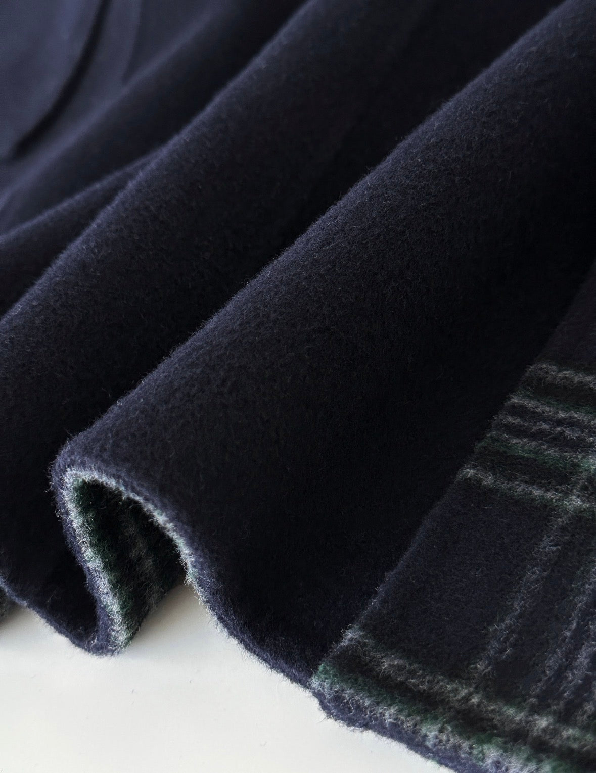 Close-up of navy double-faced wool fabric for a duffle coat, revealing a subtle green plaid interior.