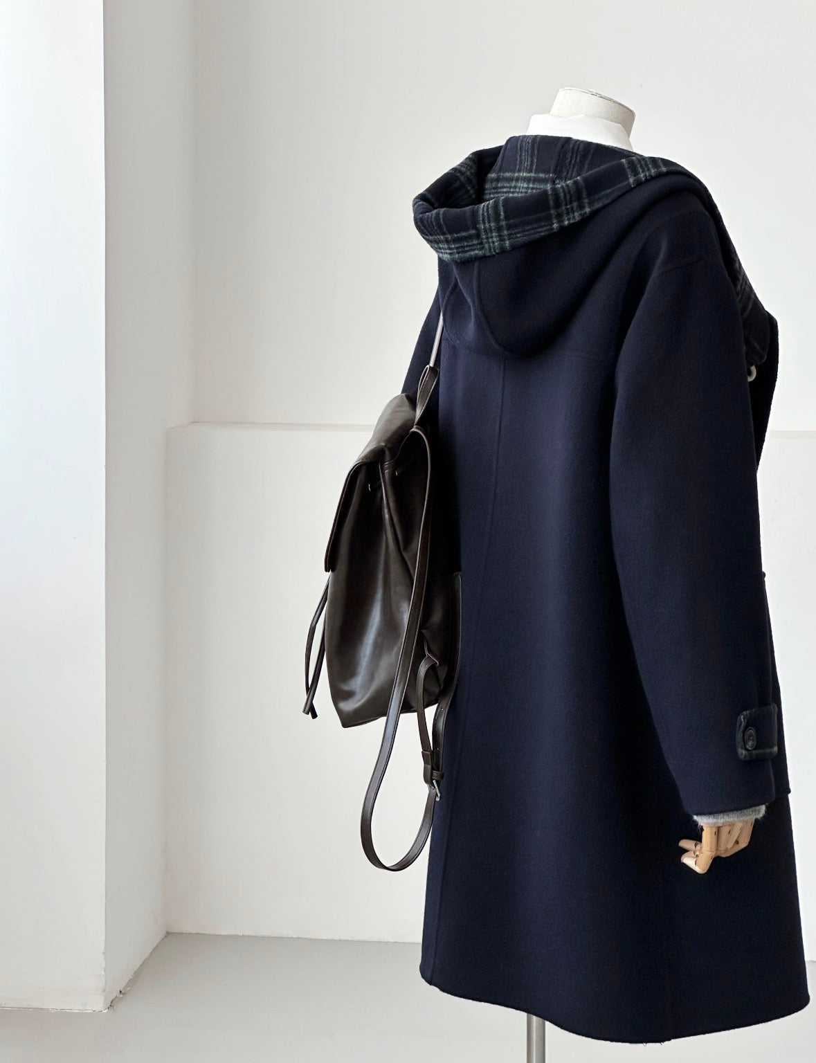 Navy Fern Hooded Duffle Coat, oversized double-faced wool, with plaid hood lining and brown backpack.