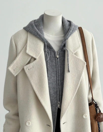Ivory tailored wool coat with a double-breasted front, convertible collar, and sharp shoulders, layered over a grey hoodie.