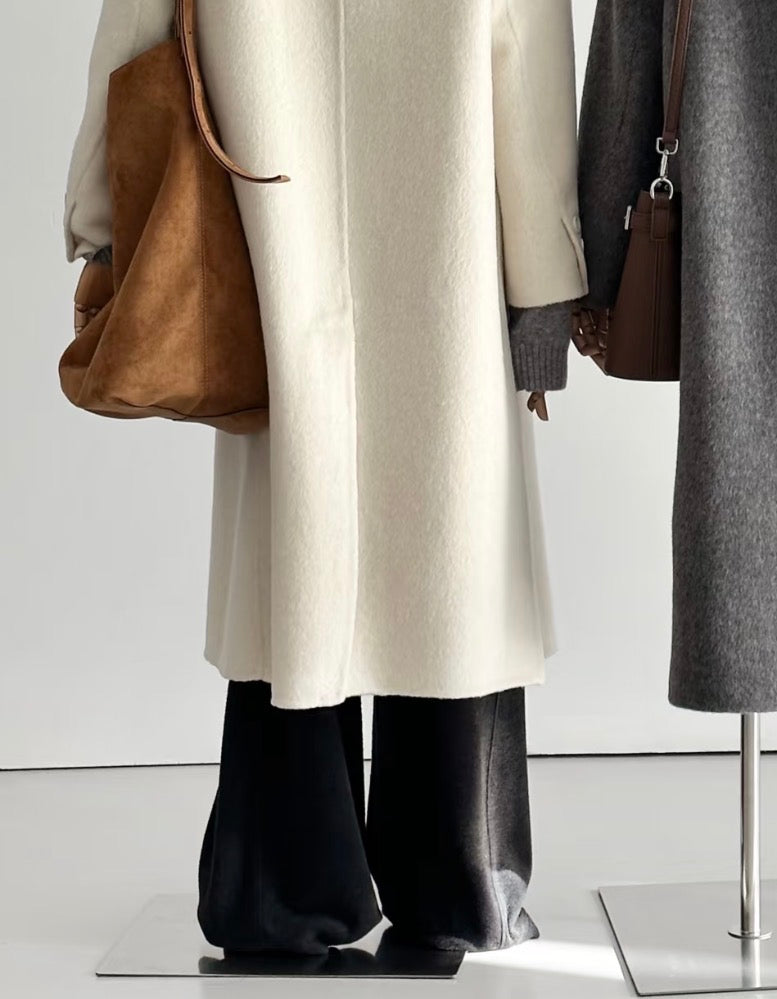 Ivory tailored wool coat with a double-breasted front, worn with black pants and a brown tote bag.