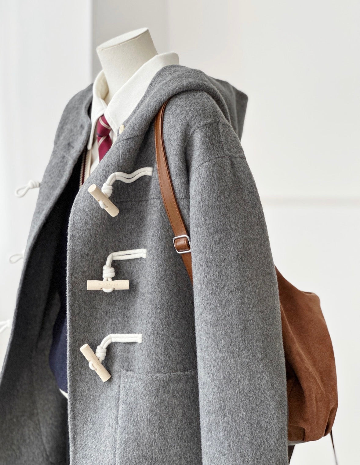 Gray Fern Hooded Duffle Coat, oversized double-faced wool, with wooden toggles and a brown shoulder bag.