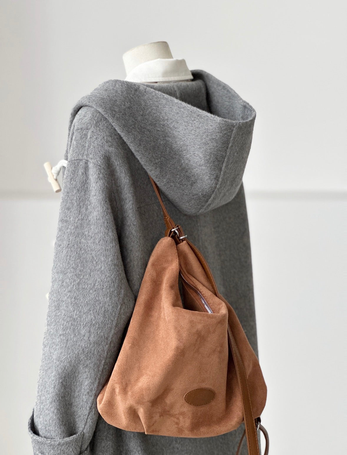 Gray Fern Hooded Duffle Coat made from double-faced wool, featuring a wooden toggle closure and a brown suede bag.