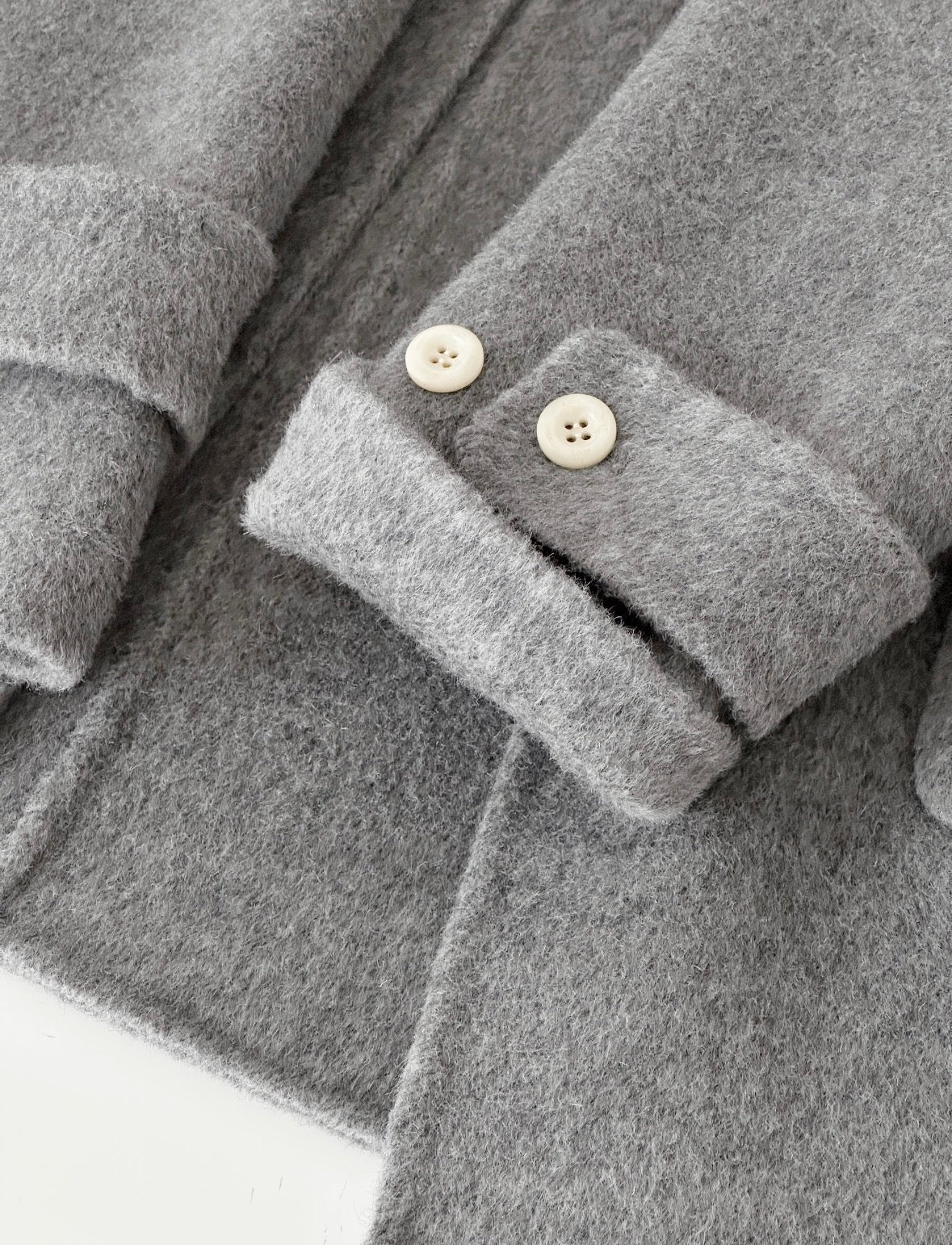 Close-up of a gray Fern hooded duffle coat sleeve with rolled cuff and two cream buttons.